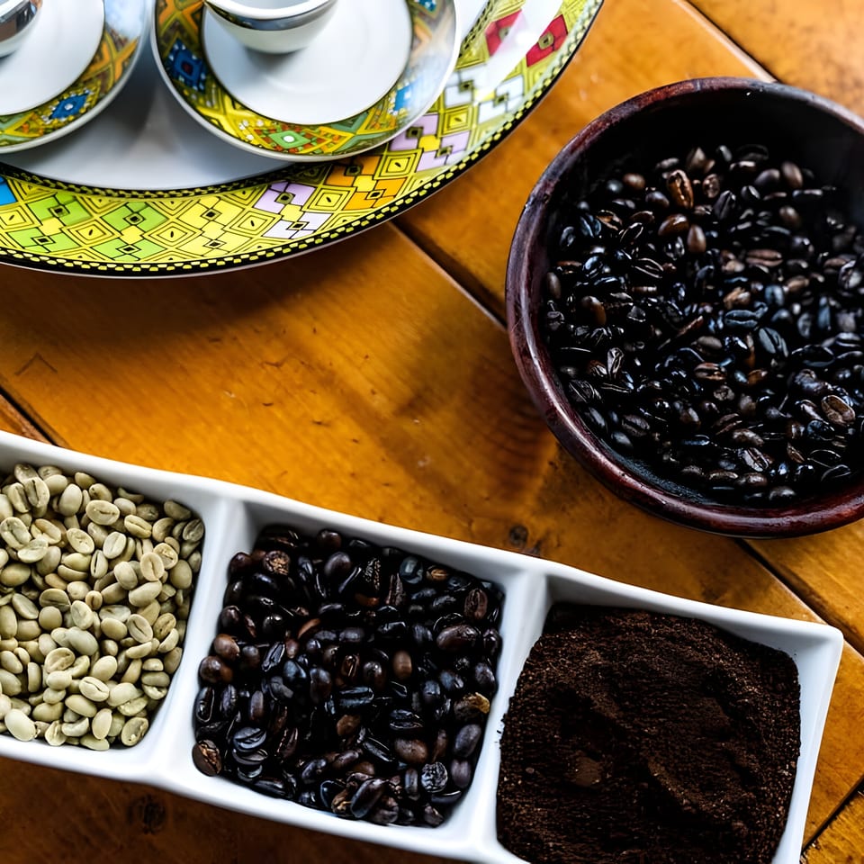 Green, roasted, and ground coffee beans displayed with traditional cups on a wooden table.