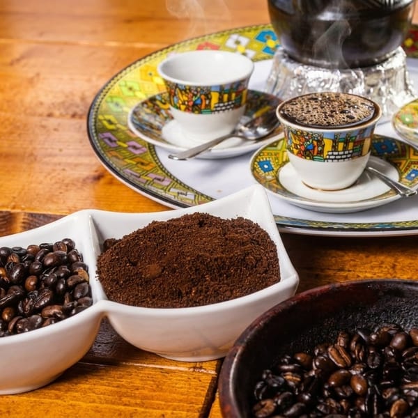 Ethiopian coffee ceremony with roasted beans, ground coffee, and steaming coffee in small cups.