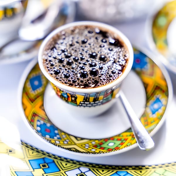 Bubbly coffee in a colorful patterned cup and saucer with a spoon on a tray.