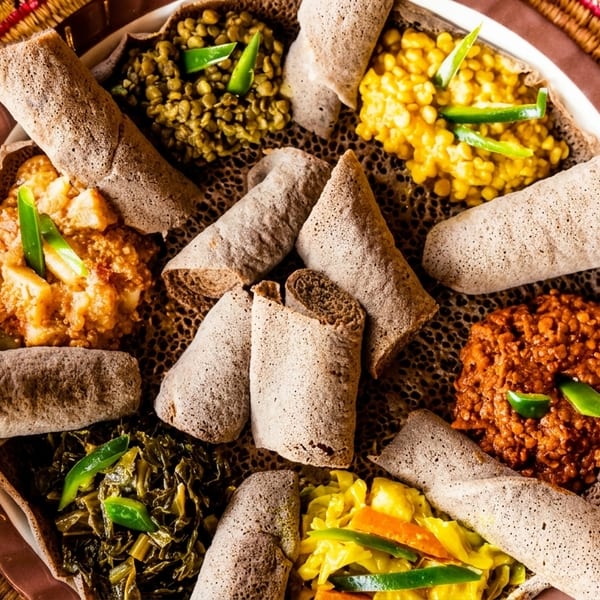 A colorful Ethiopian injera platter with various stews and vegetables, garnished with green peppers.