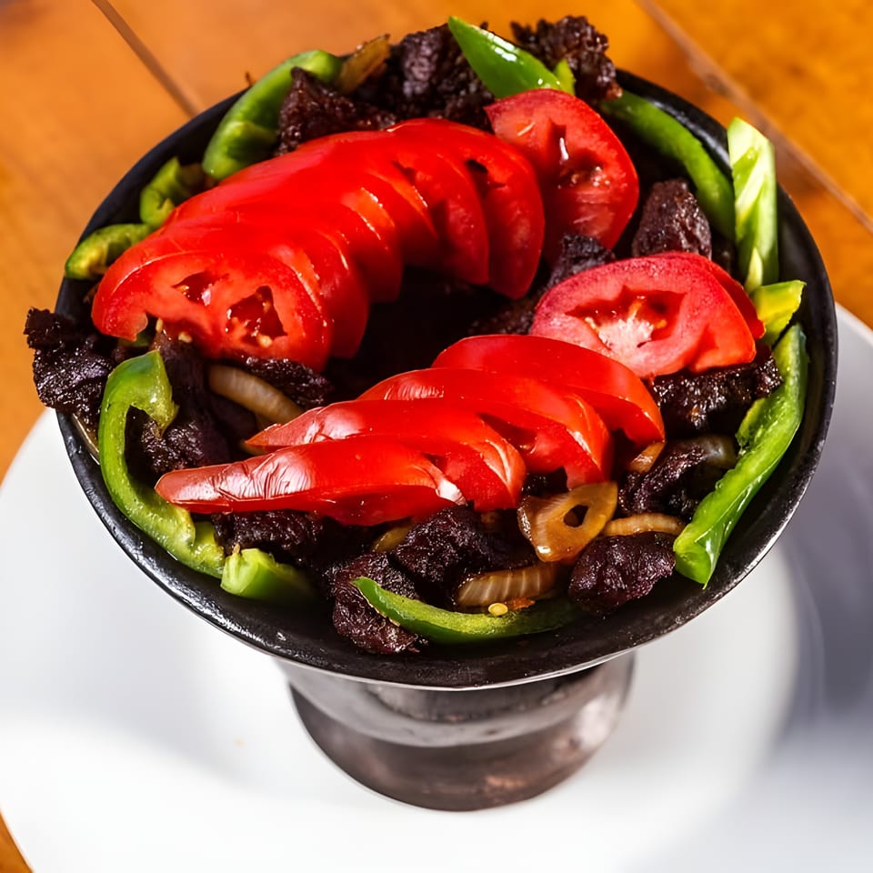 Savory meat, sliced tomatoes, green peppers, and onions served in a black bowl.