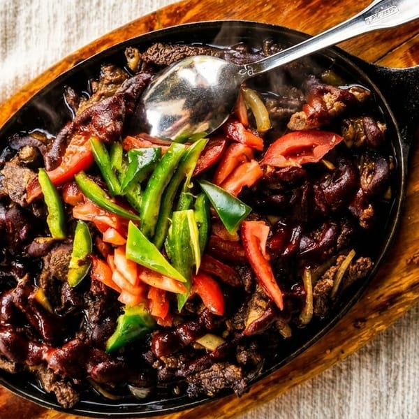 Sizzling beef fajitas with green and red peppers, onions, and a spoon in a cast iron skillet.