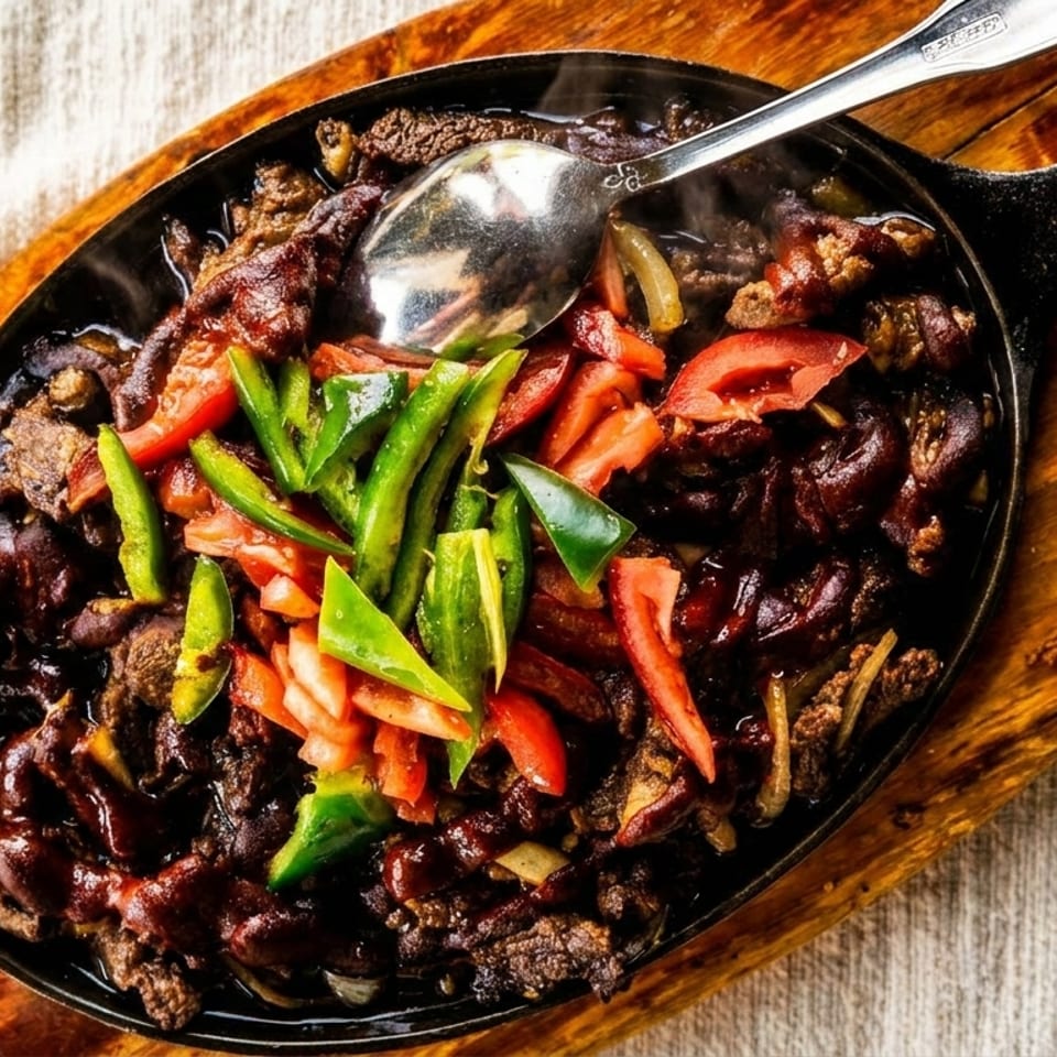 Sizzling beef fajitas with green and red peppers, onions, and a spoon in a cast iron skillet.
