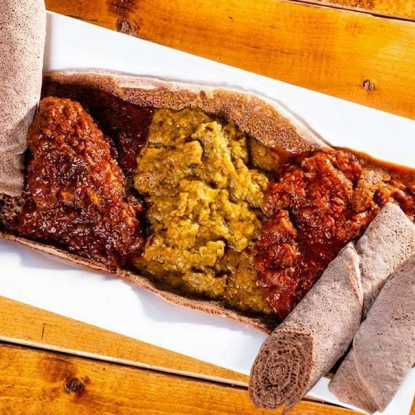 Ethiopian injera bread with three colorful stews: red, yellow, and orange, on a white plate.
