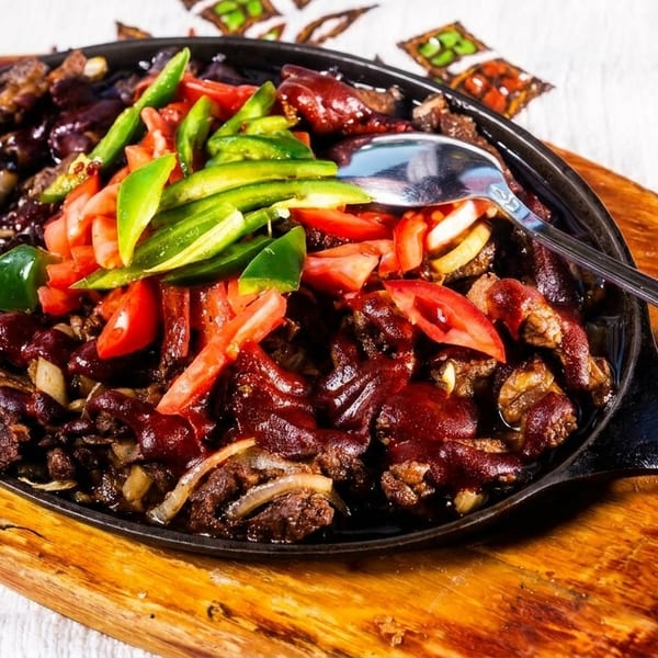 Sizzling beef fajitas with red and green peppers, tomatoes, and onions in a cast iron skillet.